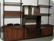 Väggmonterat
                          hyllsystem i jakarandafanér med barskåp,
                          låddel, skåp med skjutdörrar, tidningshylla
                          och hyllplan, 60-tal